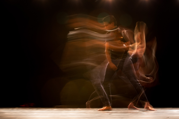 a dark artistic photo of a man to the right of the composition dancing with a motion blur suggesting slow motion and speed all at once