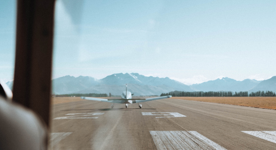 A single engine airplane on the runway ready to take off. The photo shows the plane from the back with mountains in the distance. Clear skies.